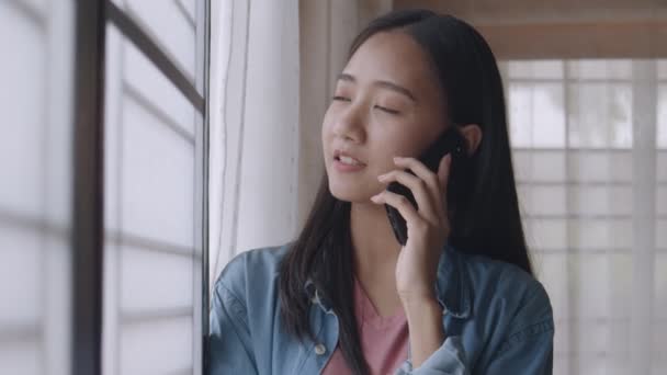 Porträt lächelnde junge Asiatin telefoniert mit Freundinnen, die im Home Office am Fenster stehen.