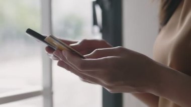 İnternetten akıllı telefon alışverişi yapan Asyalı güzel bir kadının ellerini kapat ve ofis odasının penceresinin yanında dururken kredi kartı ödemesini kullan..