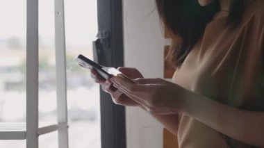 Akıllı telefon alışveriş online kullanarak güzel bir Asyalı beyaz kadın kapatın ve ofis odasında pencerenin yanında dururken kredi kartı ödeme kullanın.