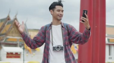 Yakışıklı Asyalı genç ve yalnız turistlerin portresi akıllı telefonları kullanarak sokakta arkadaşlarıyla görüntülü sohbet ederek Tayland tapınağı geçmişine sahip. Keyifli yaşam tarzı seyahatleri.
