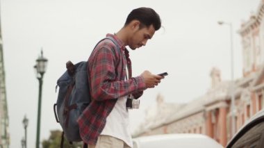 Yakışıklı turistlerin portresi, Tayland 'da caddenin yanında dururken akıllı telefon kontrol haritası kullanan Asyalı bir adam. Genç Asyalı blogcu. Keyifli bir hayat tarzı seyahatinin keyfini çıkarıyor..