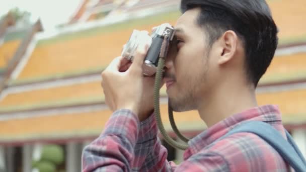 旅行や寺院タイで写真を撮るフィルムカメラを使用して歩くハンサムな若いアジアの男の観光客の肖像画 アジアの男性ブロガー幸せなレジャーライフスタイル旅行を楽しむ — ストック動画