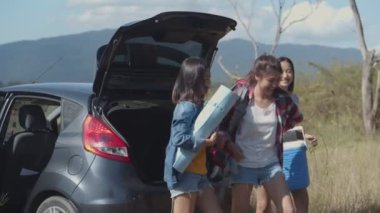 Genç Asyalı bir kadın grubu, arkadaşlarıyla yaz tatili yaparken sırt çantası ve buz soğutucusunu tutmaya yardım ediyor..