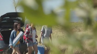 Genç Asyalı bir kadın grubu, arkadaşlarıyla yaz tatili yaparken sırt çantası ve buz soğutucusunu tutmaya yardım ediyor..