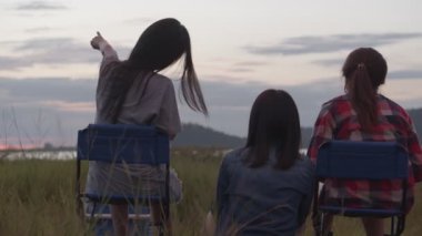 Genç Asyalı bir kadın grubu arkadaşlarıyla bir sandalyede oturup bira içerken ve gün batımını seyrederken halk parkında arkadaşlarıyla.