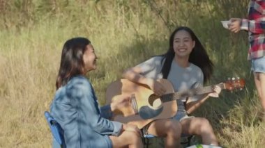 Doğada kamp yapan, gitar çalan, bira içen ve bardakları tokuşturan genç Asyalı bir grup genç kadın..