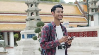 Tayland tapınağında akıllı telefon kullanarak yürüyen ve sosyal medyayı kontrol eden çekici yalnız turistler. Asyalı blogcu mutlu mesut seyahat ediyor..