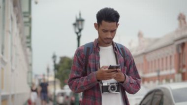 Yakışıklı turistlerin portresi, Tayland 'da caddenin yanında dururken akıllı telefon kontrol haritası kullanan Asyalı bir adam. Genç Asyalı blogcu. Keyifli bir hayat tarzı seyahatinin keyfini çıkarıyor..