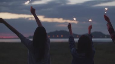 Bir grup genç Asyalı kadın ellerinde maytap tutarak yeni yılı kutluyorlar doğada kamp yapıyorlar birlikte bira içerek eğleniyorlar..