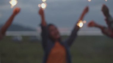 Bulanık bir Asyalı genç kadın grubu elinde maytap tutarak yeni yılı kutluyor arkadaşlarıyla doğada kamp kuruyor birlikte bira içip eğleniyorlar..