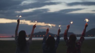 Bir grup genç Asyalı kadın ellerinde maytap tutarak yeni yılı kutluyorlar doğada kamp yapıyorlar birlikte bira içerek eğleniyorlar..