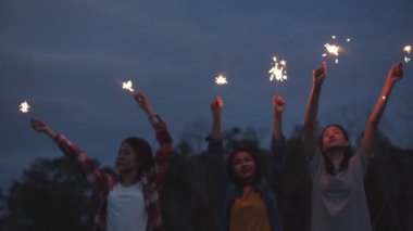 Bir grup genç Asyalı kadın ellerinde maytap tutarak yeni yılı kutluyorlar doğada kamp yapıyorlar birlikte bira içerek eğleniyorlar..