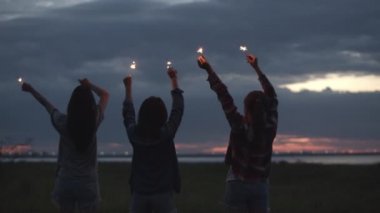 Bir grup genç Asyalı kadın ellerinde maytap tutarak yeni yılı kutluyorlar doğada kamp yapıyorlar birlikte bira içerek eğleniyorlar..