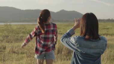 Genç dişiler akıllı telefondan fotoğraf çekerken gün batımında birlikte bir yaz seyahati yapıyorlar. Bir grup Asyalı genç arkadaşın yaşam tarzı tatil tatiline çıkıyor. Bir dağ geçmişine sahip olmak.