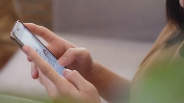 Yakın el ele tutuşan Asyalı genç iş kadını elinde daktilo ile oturma odasındaki bir kanepede otururken sosyal medya üzerinden akıllı bir telefonla bilgi aktarıyor..