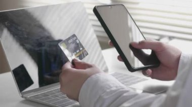 Asyalı işadamı cep telefonunu tutuyor ve ofisteki koltukta otururken kredi kartı ödemesini akıllı telefondan yapıyor..