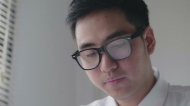 Asyalı işadamı ofiste bir kanepede otururken kendini yorgun hissediyor ve pencereden dışarı bakıyor..