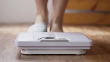 Genç Asyalı kadının, evdeki oturma odasında vücut ağırlığını tartarken yakın plan..