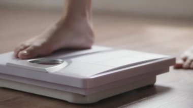 Genç Asyalı kadının, evdeki oturma odasında vücut ağırlığını tartarken yakın plan..