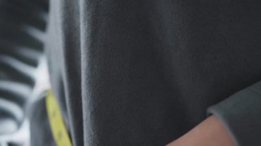 Oturma odasında dururken, belini bantla ölçen Asyalı kadını kapat..