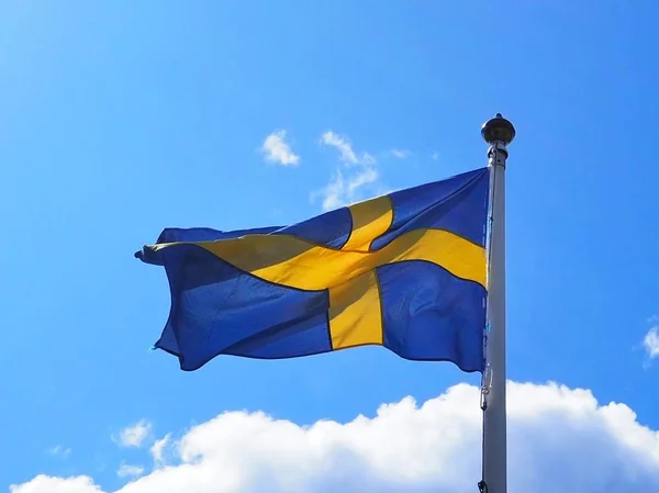 The swedish flag blowing in the wind. The flag of sweden against a blue sky with clouds on a windy day in summer.