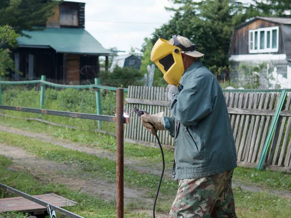 a man works with a welding machine in the backyard in the summer in sunny weather