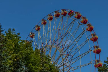 Dönme dolap ve yaz renkleri. Dansdaki dönme dolap Ağaçların arasından geçiyor.