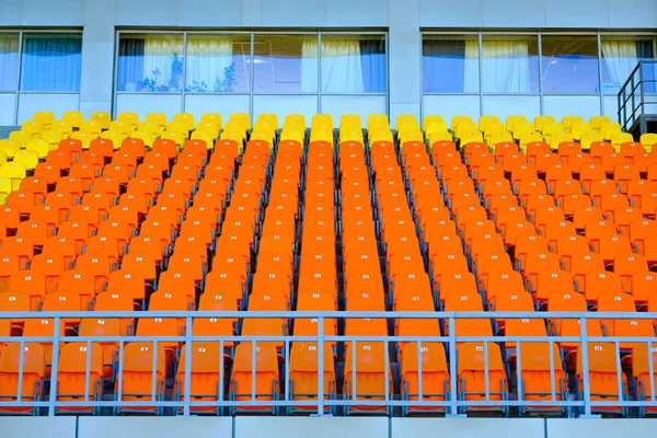 Reihen leerer gelber und orangefarbener Plastiksitze in einem Stadion — Stockfoto