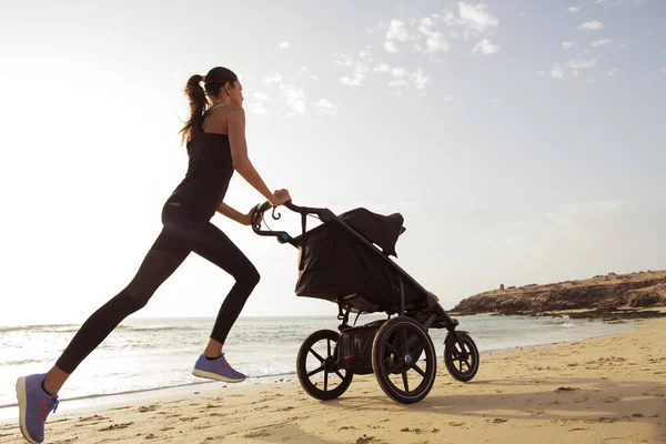 Young mom is running with stroller on the beach.