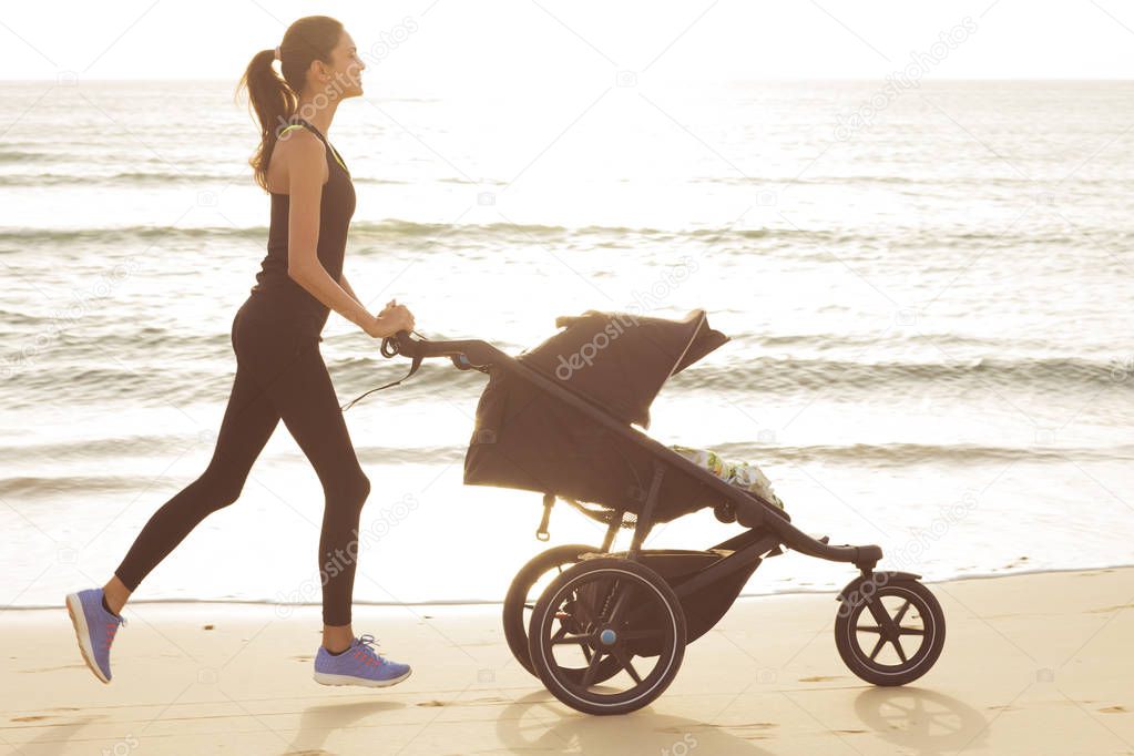 Young mom is running with stroller on the beach.