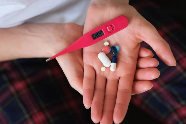 Close up of female hands holding a handful of medicine and digital thermometer.