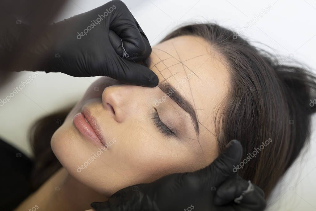 Beautician in the saloon doing the perfect architecture of eyebrows.