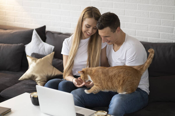 Young couple sitting with a red hair cat in a living room.