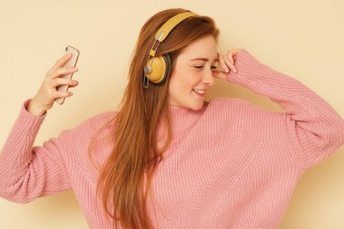 Genç taze güzellik ateş, zencefil saçlı enerji kız dolu müzik dinlerken ve onu telefonda izlerken.