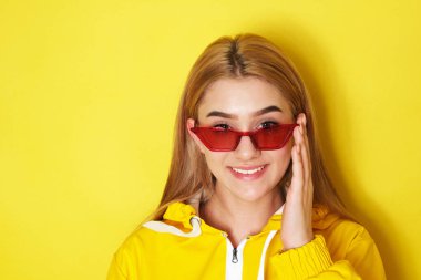 Sarı ceketli ve kırmızı gözlüklü güzel kız kameraya bakıyor.