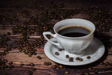 Bir fincan kahve ahşap masada kahve çekirdekleri ile çevrili.