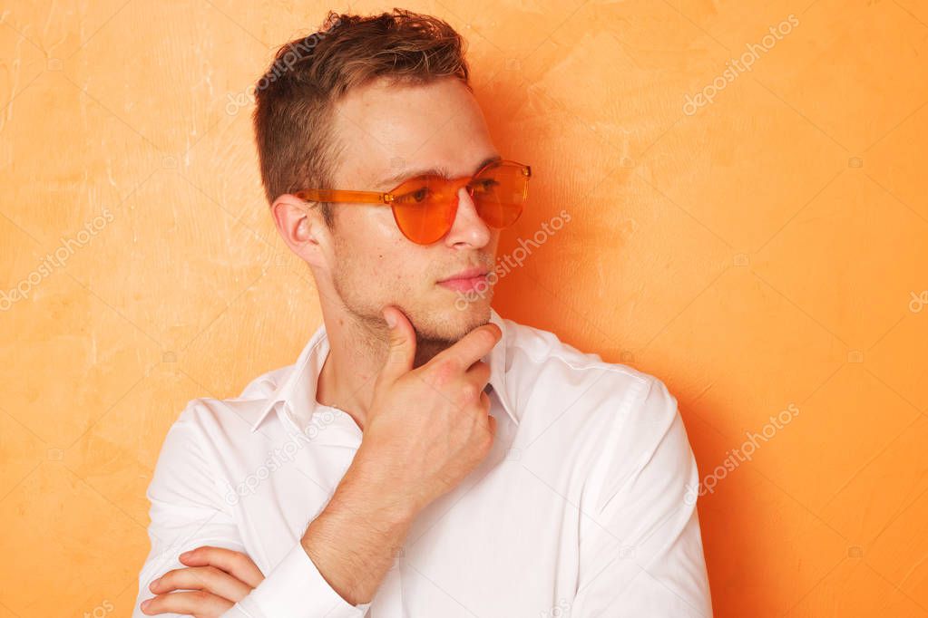 Young men with orange eyeglasses on orange background.