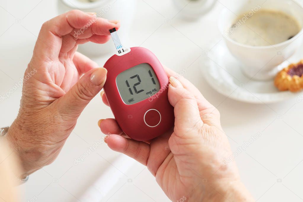 Older woman sitting next to table and examining her glucose level.