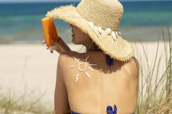 Beautiful woman knows how safety taking sun. She is wearing a hat and applying a sun cream.