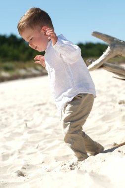 Beyaz keten gömlek giyen sevimli küçük bebek sahilde oynuyor,