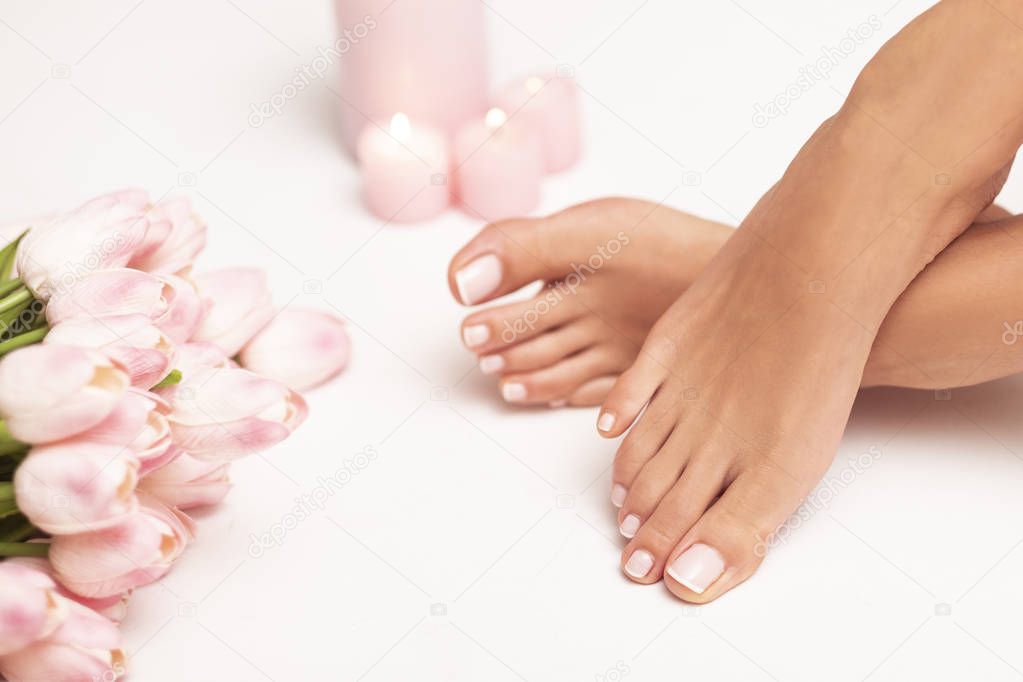 The picture of female legs and hands after pedicure and manicure. Legs are surrounded by pink tulips and candles.