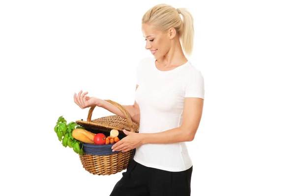 幸せなブロンドの女性は 健康的な野菜や果物の完全なウィッカーバスケットを保持しています 彼女は健康で活力を保つために何が重要かを知っている — ストック写真