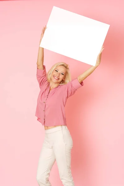Blonde woman in pink shirt is holding up a white banner with information.