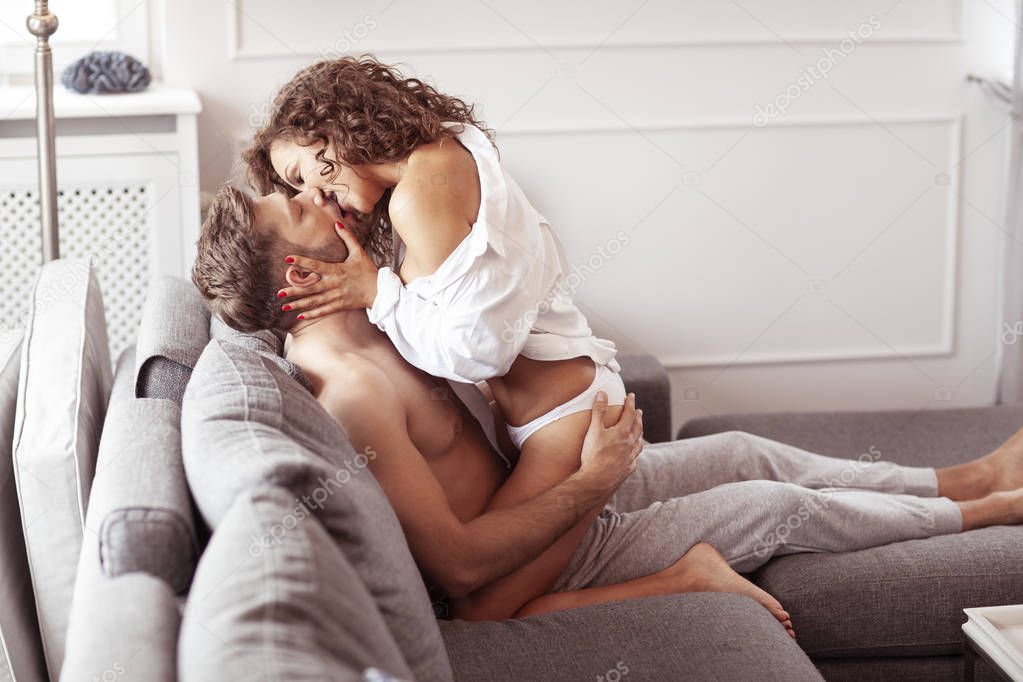 Intimate couple kissing on sofa and getting undress.