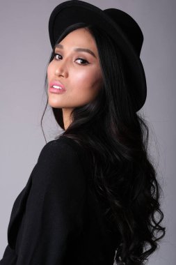 Siyah paltolu ve şapkalı Asyalı mankenin şehvetli portresi.