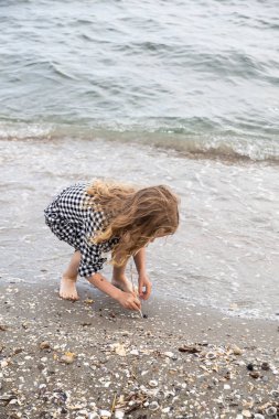 Güzel küçük kız denizde açık gökyüzü ve sakin su ile huzurlu bir yaz gününde kum oynarken
