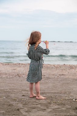 Güzel küçük kız denizde açık gökyüzü ve sakin su ile huzurlu bir yaz gününde kum oynarken