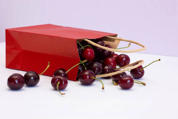 Red paper bag with burgundy cherries on a white background on the table, eco-friendly products — Stock Photo, Image