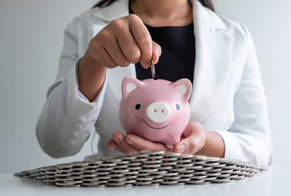 woman hand putting coin into pink piggy bank with coins bunker, step up protect business to success and saving for retirement concept
