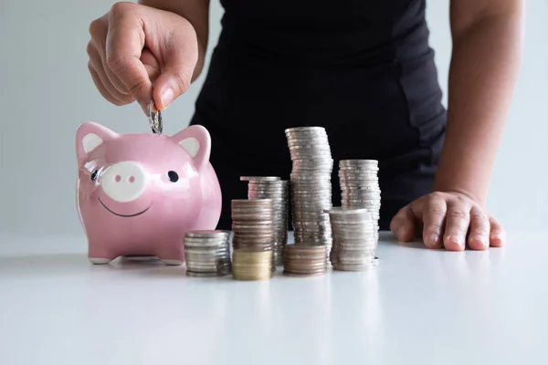 one woman putting coin in pink piggy bank with coins pile, step up growing business to success and saving for retirement concept